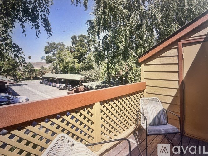 A balcony with a chair and a fan overlooking a parking lot.