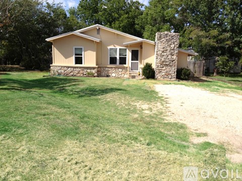 A house with a stone chimney is surrounded by a grassy yard.