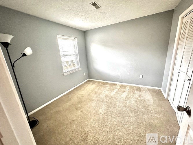 A room with a carpeted floor, a window with blinds, and a door with a handle.