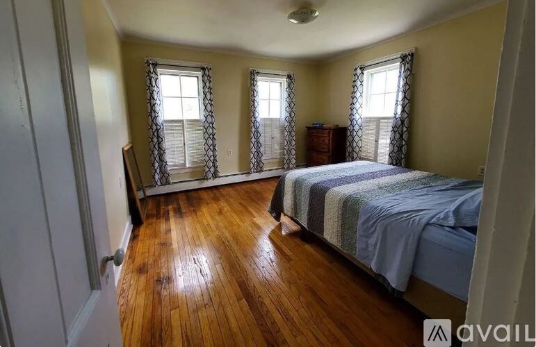 A bedroom with a bed, dresser, and window with curtains.