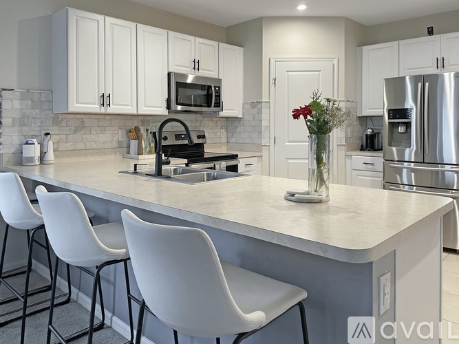 A kitchen with a white countertop and white chairs.