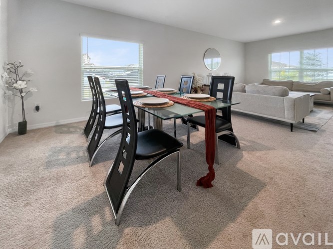 A modern dining room with a glass table and chairs, a sofa, and a vase of flowers.