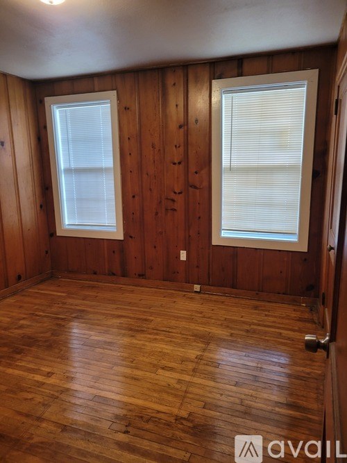 A room with wooden walls and floor and two windows.