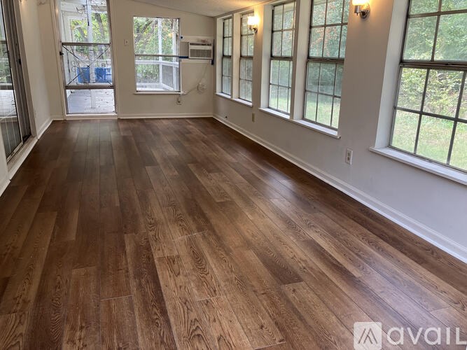 A room with wooden flooring and windows on one side.