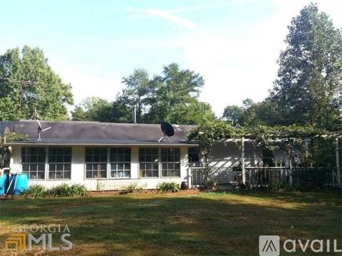 A white house with a black roof is surrounded by trees.