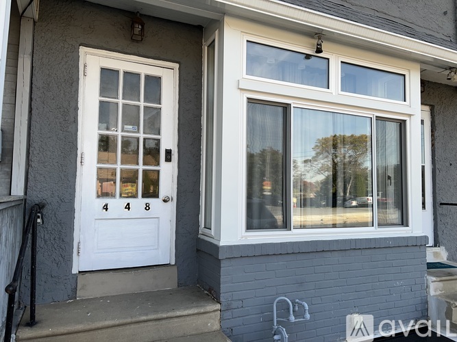 A white door with the numbers 448 on it is on the left and a window with a reflection of trees is on the right.