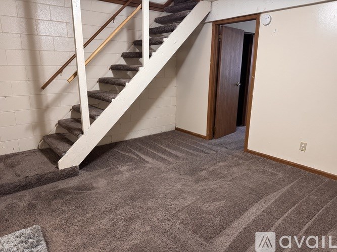 A staircase with a wooden handrail and a carpeted floor leading to a door.