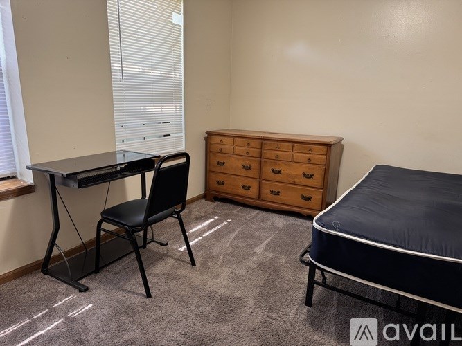 A room with a bed, desk, chair, and drawers.
