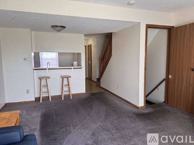 A living room with a bar stool and a grey carpet.