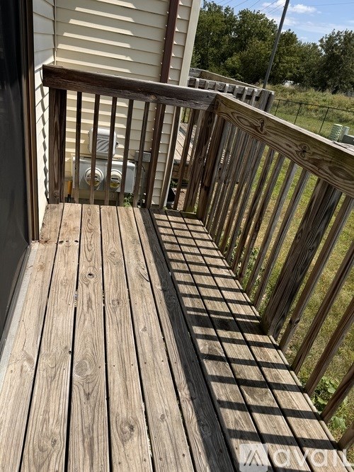 A wooden deck with a railing and a car in the background.