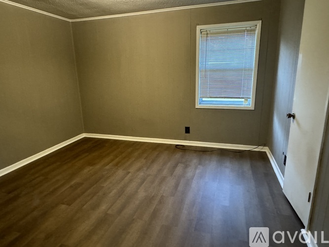 A room with wooden flooring and a window with blinds.