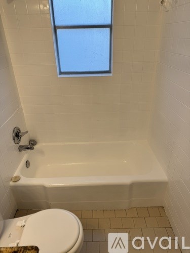 A white bathroom with a toilet, tub, and window.