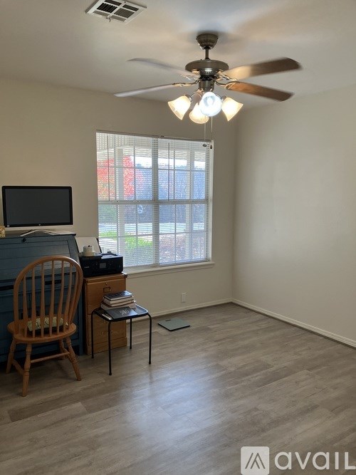 A room with a ceiling fan, a chair, a desk, and a window.