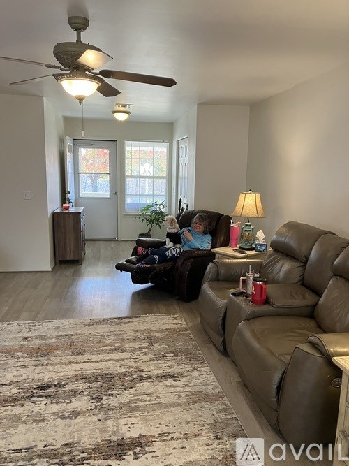 A woman is sitting on a brown leather couch in a living room.
