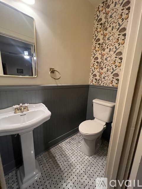 A white pedestal sink with a gold faucet is in a bathroom with a toilet and a mirror.