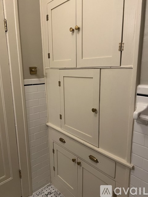 A white cabinet with a gold handle is in a bathroom.