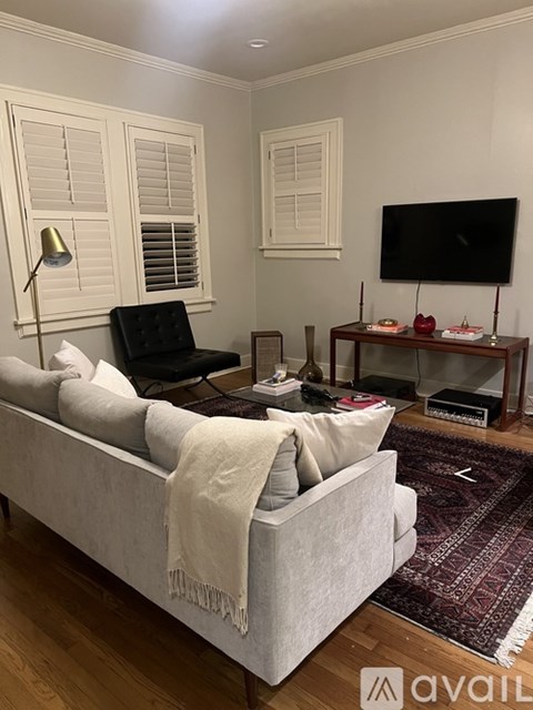 A living room with a grey couch, a black chair, a white lamp, a flat screen TV and a rug.