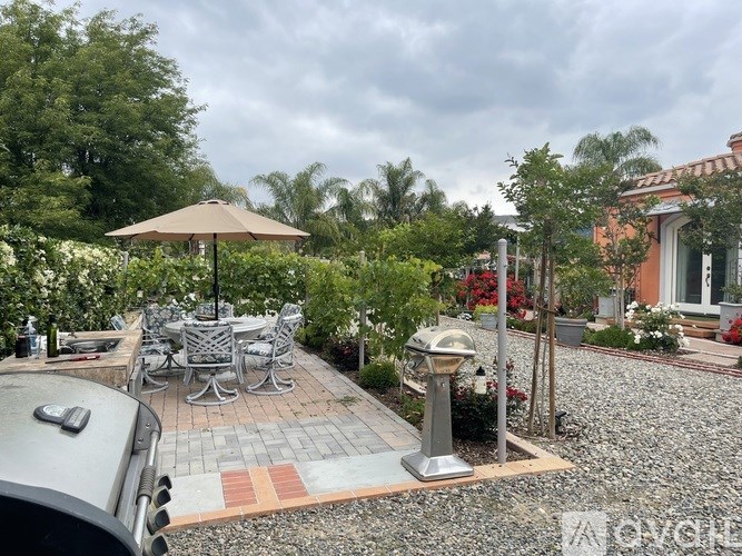 A patio with a table and chairs is surrounded by greenery.