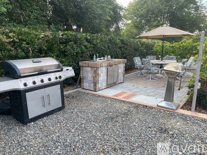 A BBQ grill is on a gravel area next to a table and chairs.