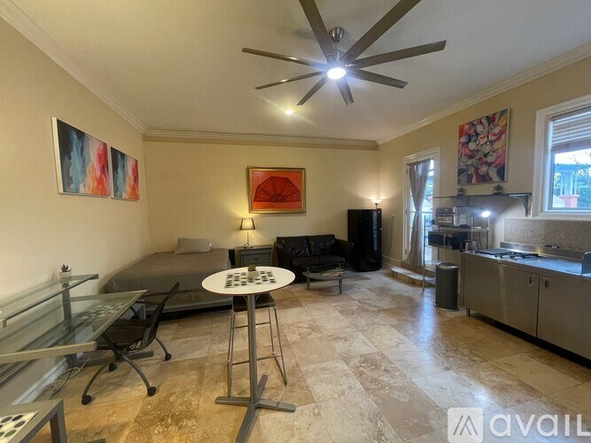 A living room with a black couch, a glass table, and a ceiling fan.