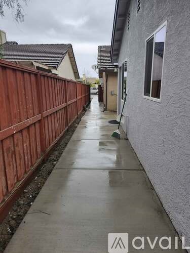 A wet sidewalk in front of a house with a wooden fence.