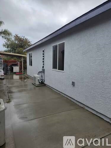 A white house with a grey roof and a grey wall with a window and a door.