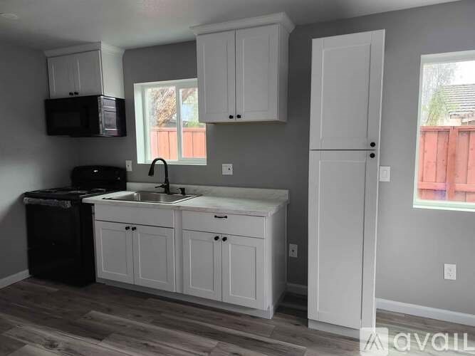 A kitchen with white cabinets and a black trash can.