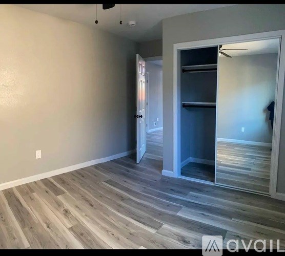 A room with a wooden floor and a white wall with a doorway leading to another room.