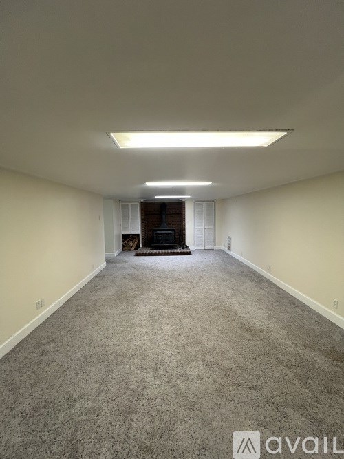 A spacious room with carpeted floor and a fireplace in the background.