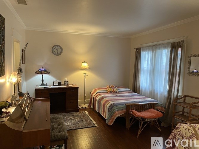 A bedroom with a bed, desk, chair, and a clock on the wall.