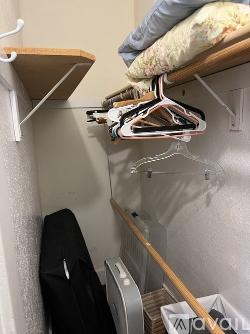 A small closet with a hanging shelf and a bed.