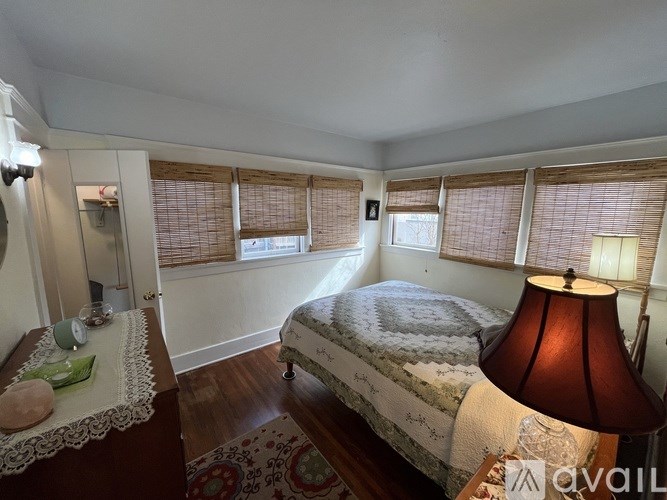 A bedroom with a bed, a nightstand with a lamp, and a window with blinds.