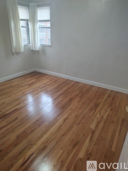 A room with wooden flooring and a window with white curtains.