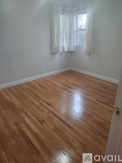 A room with wooden flooring and a window with white curtains.