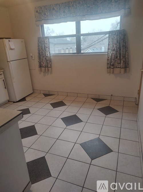 A kitchen with a white fridge and a window with curtains.