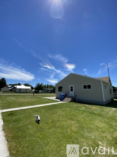A person is walking on a grassy field in front of a building with a clear blue sky above.