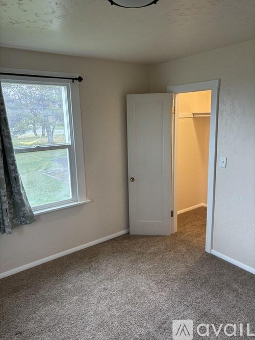 A room with a carpeted floor, a window with a curtain, and a door leading to another room.