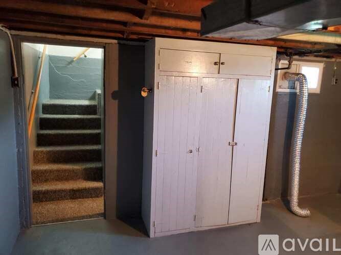 A white cupboard with a door open is in a room with a staircase.