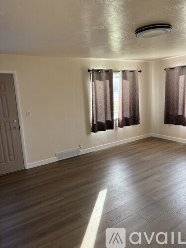 A room with wooden flooring and a window with curtains.