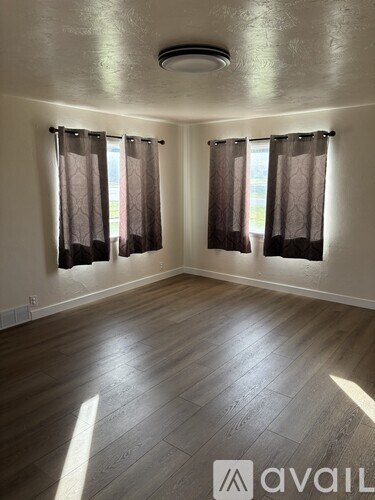 A room with wooden flooring and two windows with curtains.