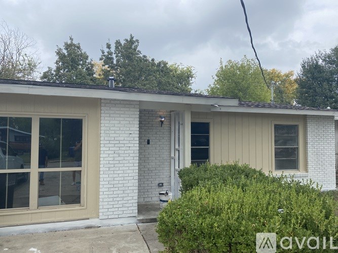 A white house with a grey roof and a bush in front.
