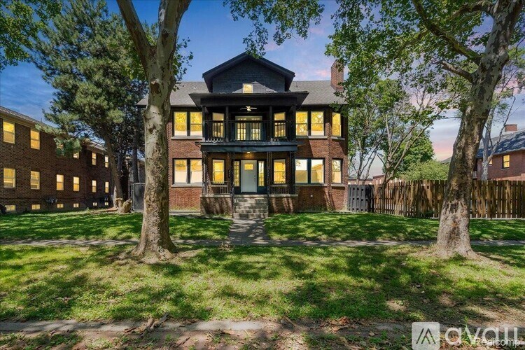 A large house with a black roof and yellow windows is surrounded by trees.