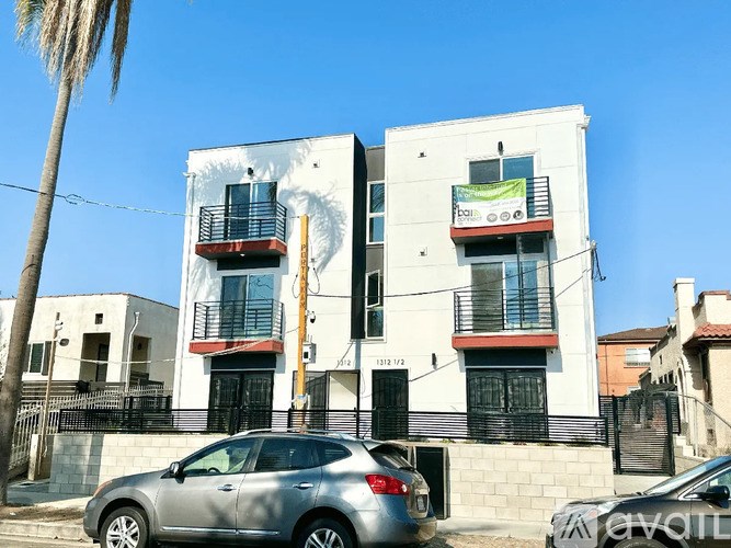 A silver car is parked in front of a white building with a red awning.