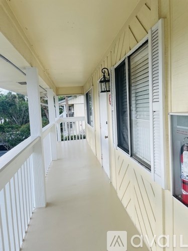 A long white balcony with a white railing and a white wall with a window.