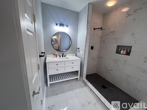 A bathroom with a mirror, a vanity with drawers, and a shower area.