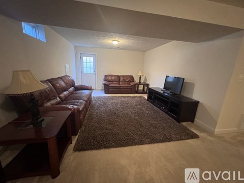 A living room with a brown leather couch, a brown rug, and a flat screen TV.
