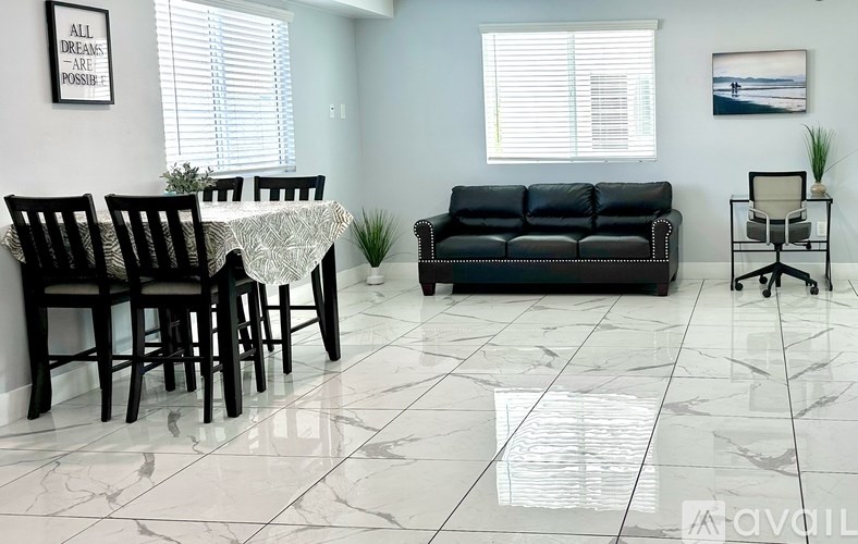 A living room with a black couch, a dining table with chairs, and a small potted plant.