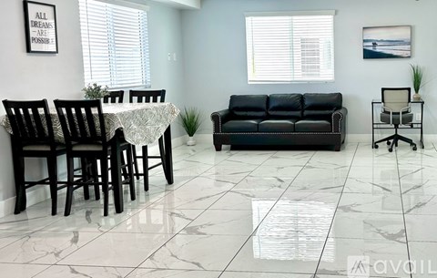 A living room with a black couch, a dining table with chairs, and a small potted plant.