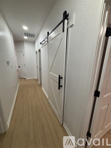 A hallway with white walls and wooden floors leading to a white door.