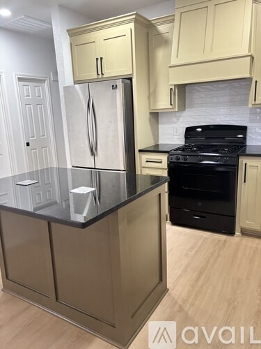 A kitchen with a black countertop and a stainless steel refrigerator.